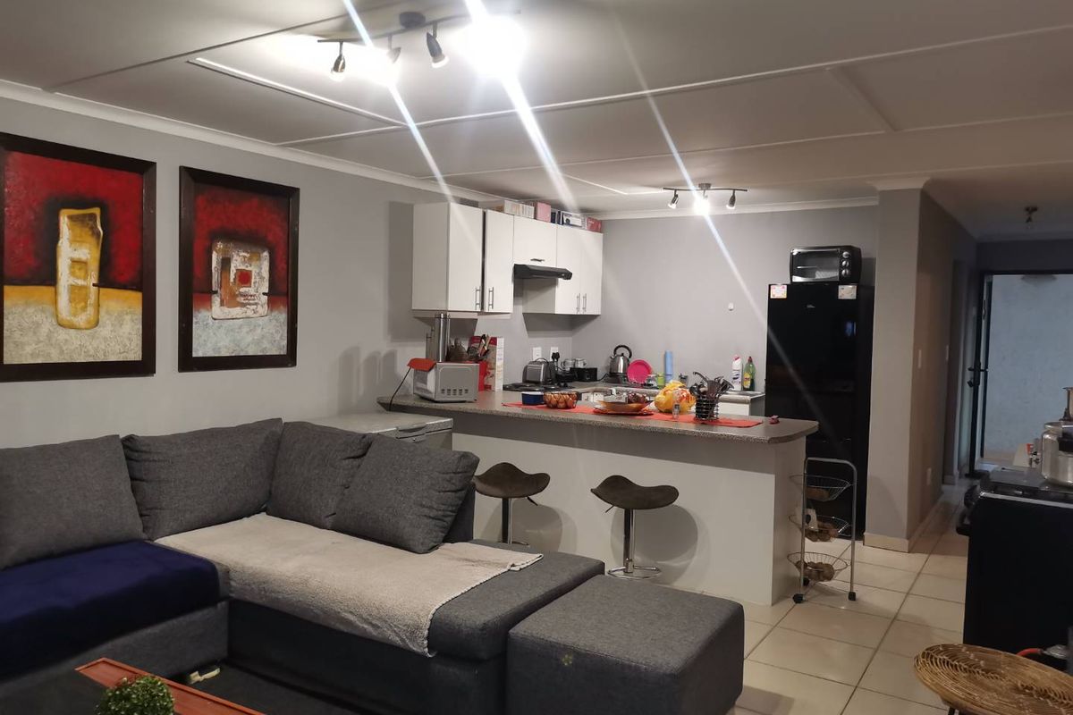 Open-plan living area featuring a kitchen with white cabinetry, breakfast bar, and tiled flooring, seamlessly connected to the lounge space.