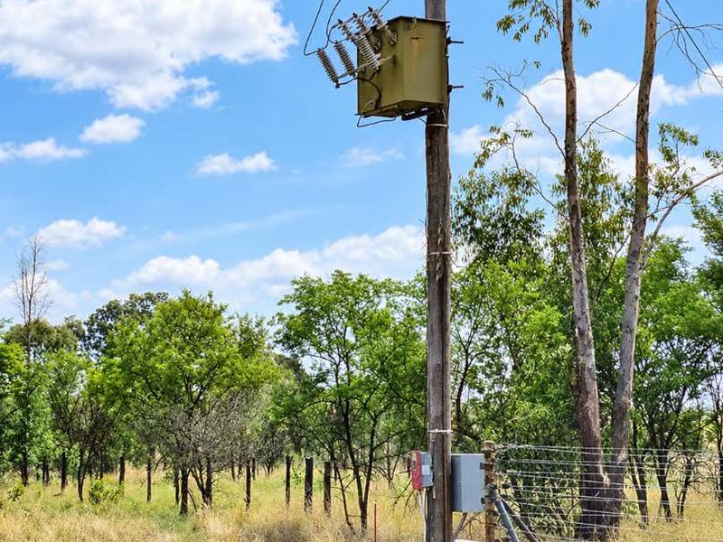 An outdoor utility pole featuring an electrical transformer and associated distribution equipment, situated within a fenced rural landscape.