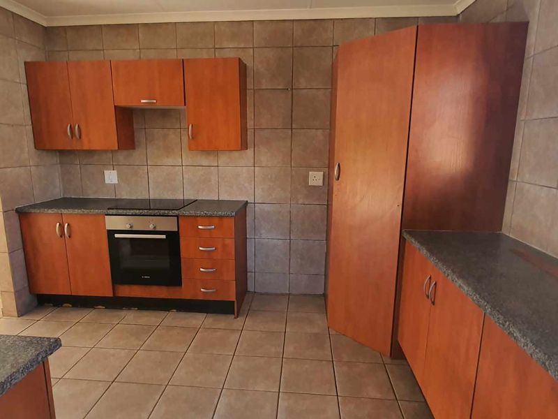 A functional kitchen featuring wooden cabinetry, dark laminate countertops, built-in oven and hob, and tiled splashbacks in an open-plan layout.