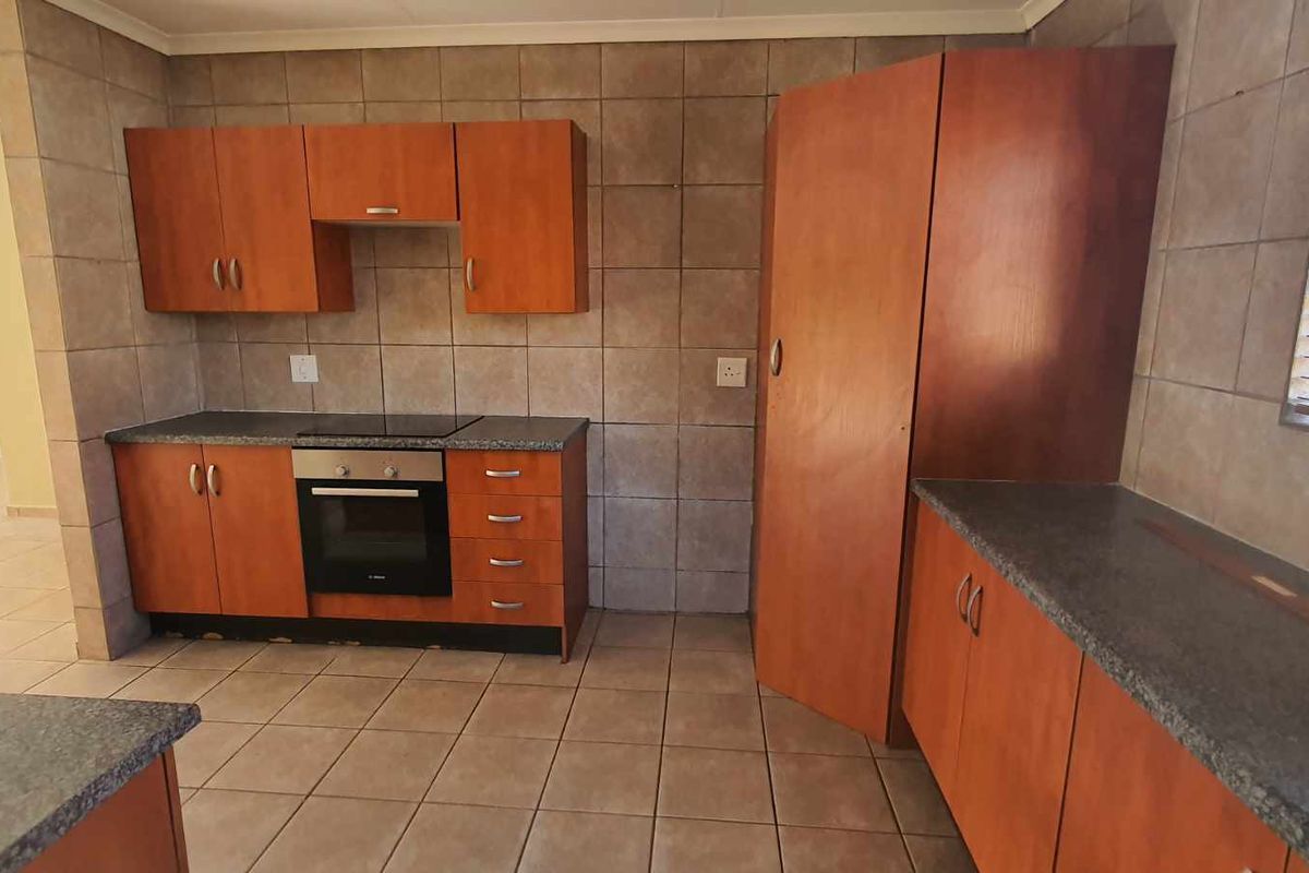 A functional kitchen featuring wooden cabinetry, dark laminate countertops, built-in oven and hob, and tiled splashbacks in an open-plan layout.