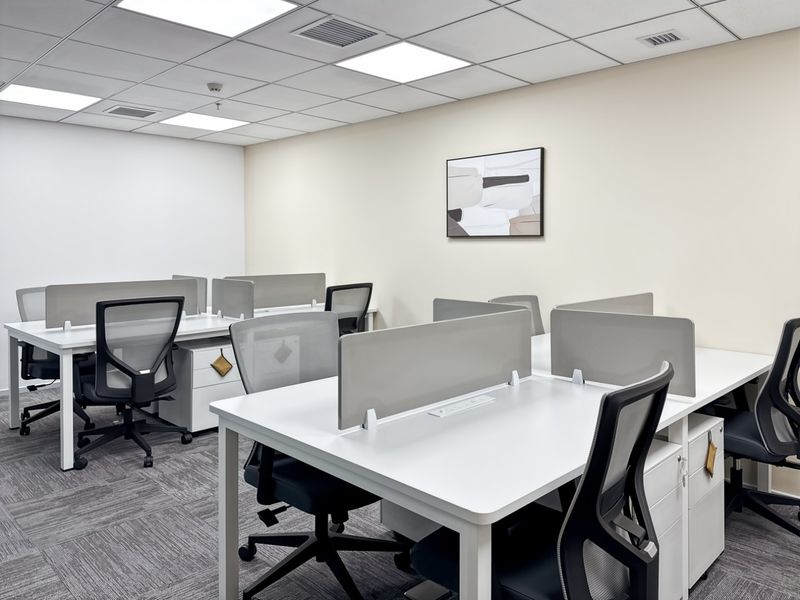 A modern, well-lit office space featuring a suspended ceiling, recessed lighting, and professional carpet tiles, configured with multiple workstations.