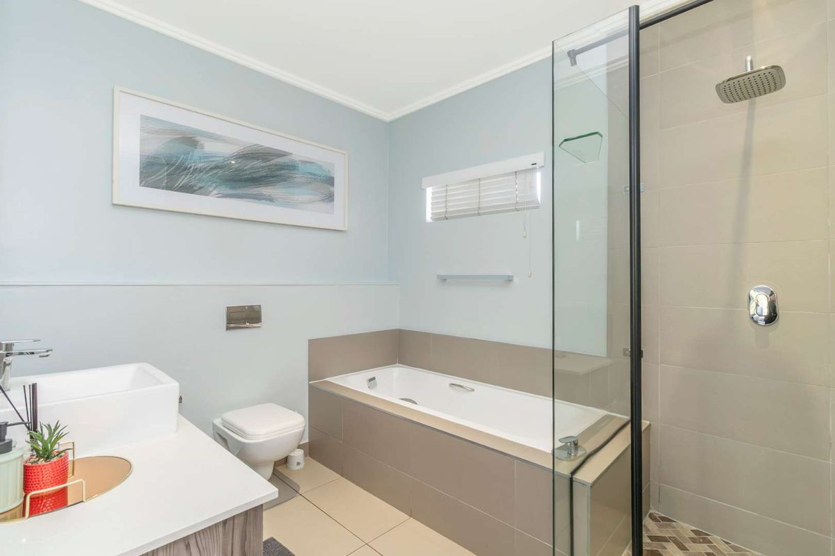 Modern bathroom featuring a sleek built-in bathtub, separate glass-enclosed shower with rain head, wall-mounted toilet, and a contemporary vanity with countertop basin.