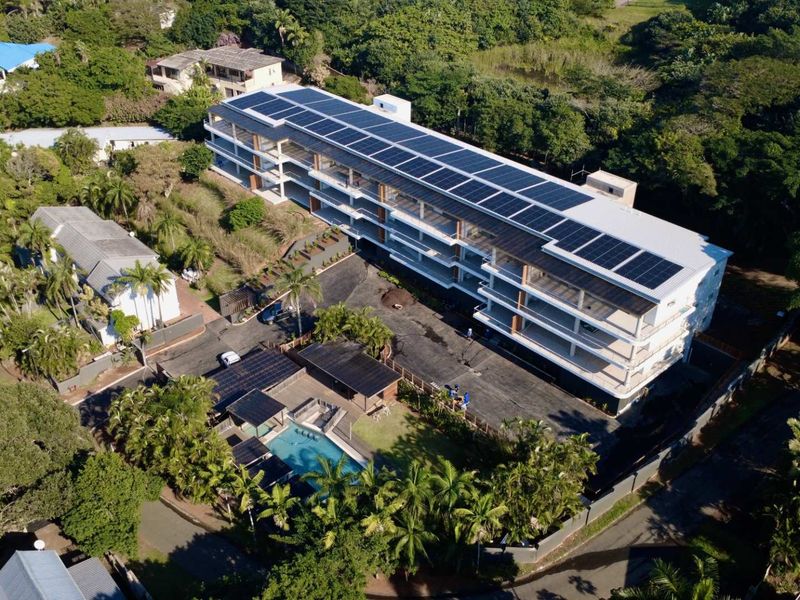 Aerial view of the apartment complex featuring extensive rooftop solar panels, a swimming pool, and landscaped grounds.
