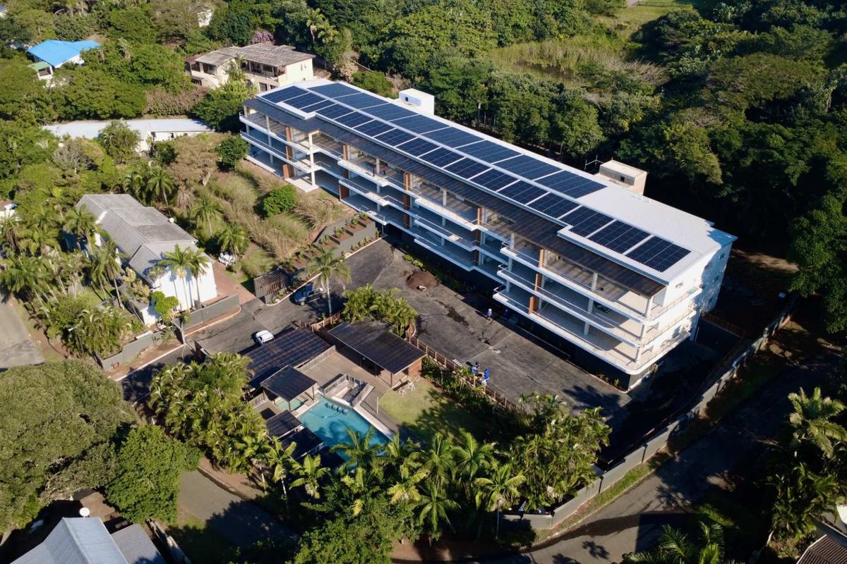 Aerial view of the apartment complex featuring extensive rooftop solar panels, a swimming pool, and landscaped grounds.