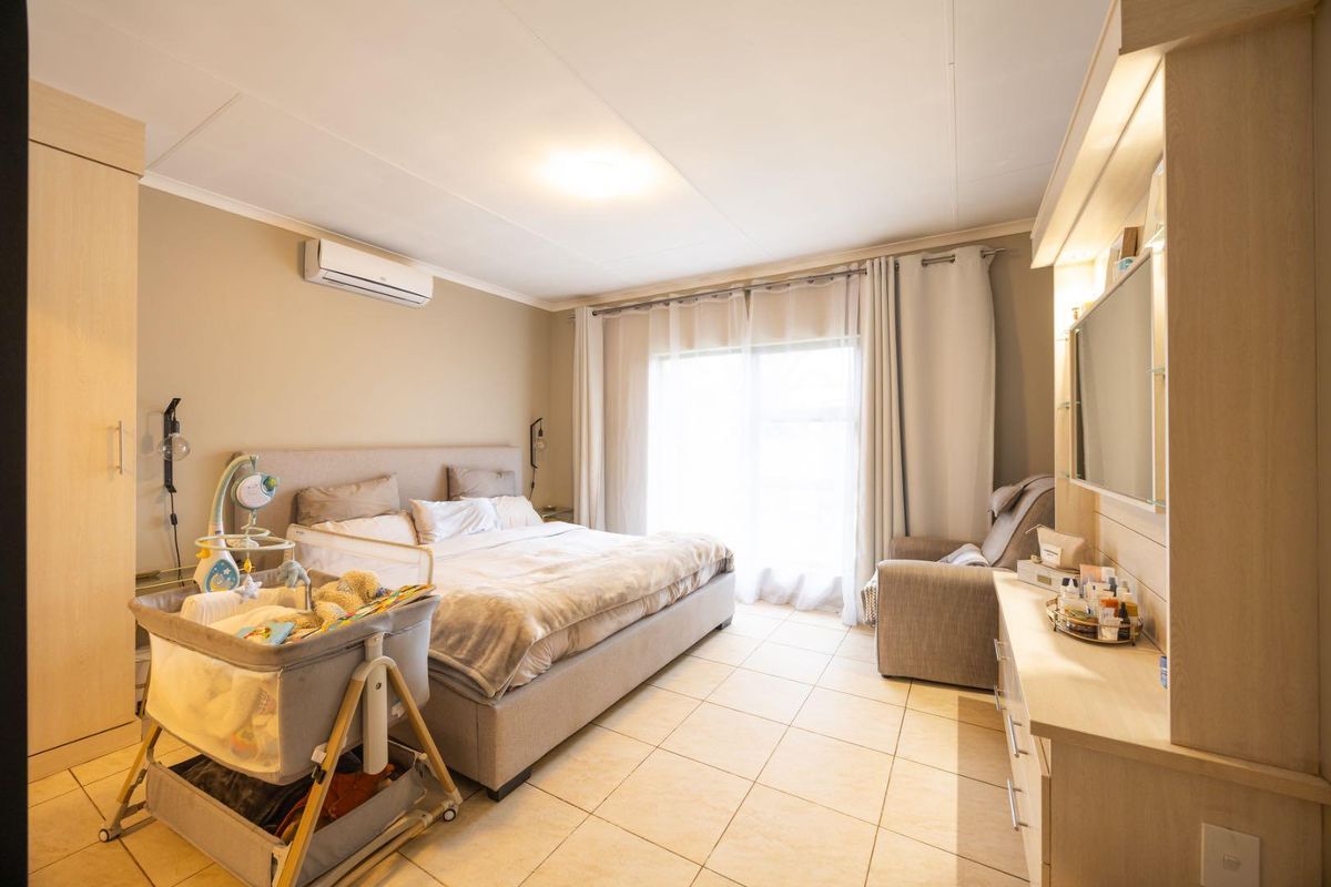 Spacious bedroom featuring tiled flooring, built-in cupboards, a vanity unit, and a split-system air conditioner with access to a patio through sliding doors.