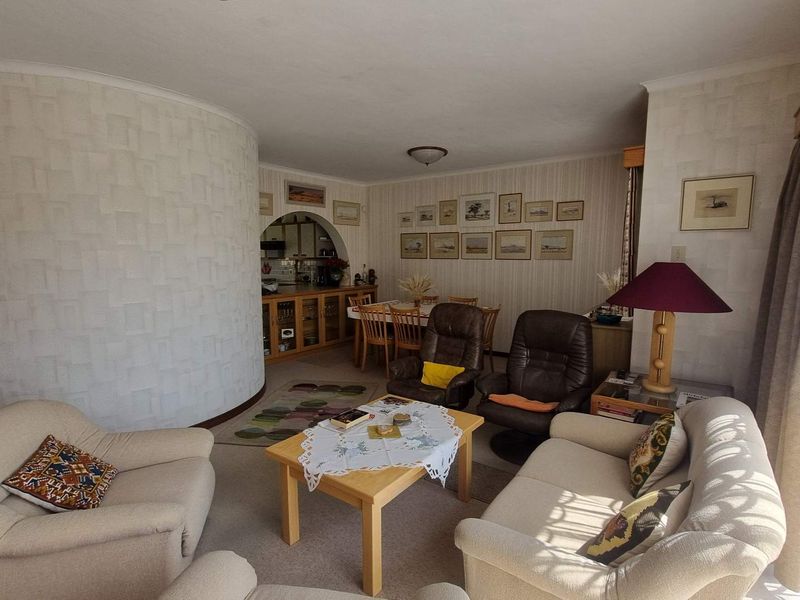Open plan living and dining area featuring a distinctive curved wall, arched entryway to the kitchen, and neutral carpeting throughout.