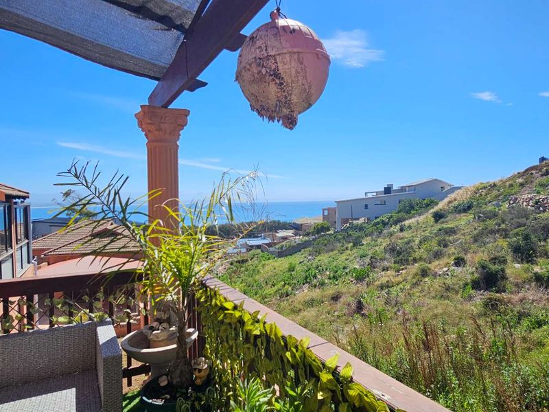 An elevated balcony featuring a timber pergola and decorative column, offering scenic coastal and hillside views.