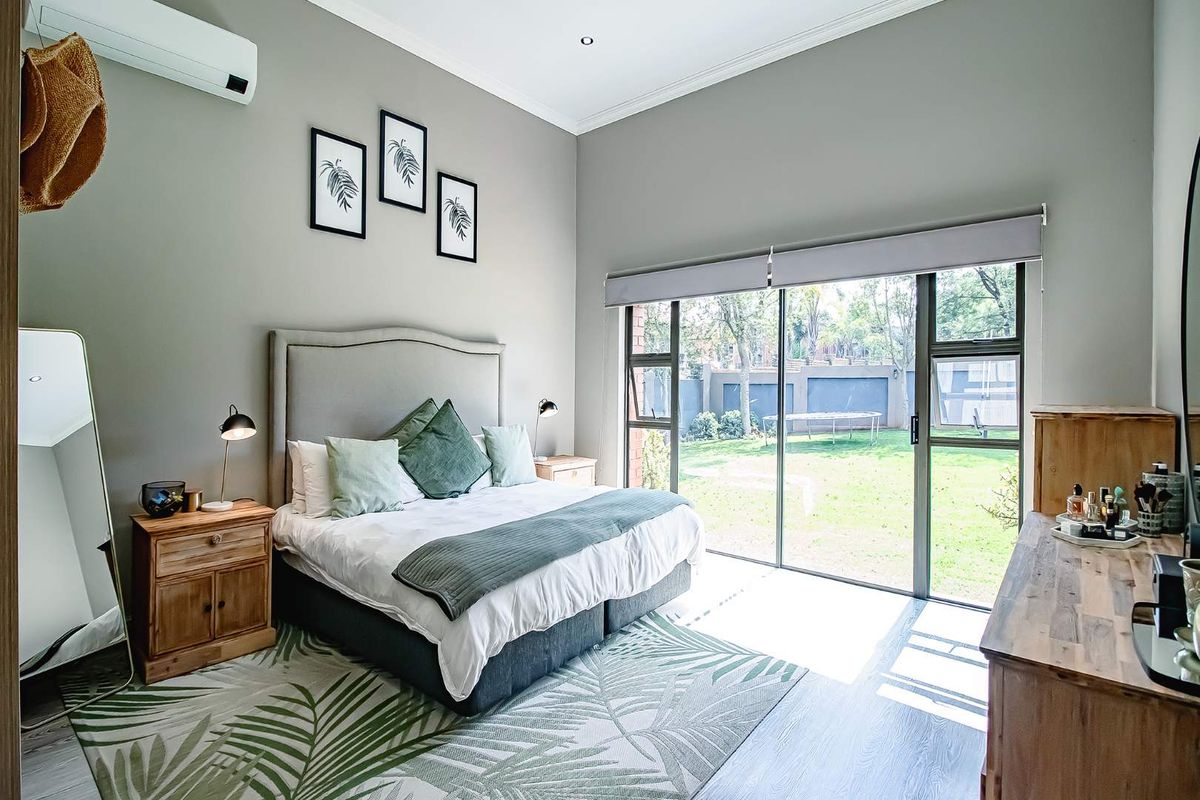 A well-maintained bedroom featuring laminate flooring, recessed lighting, a split-system air conditioner, and large sliding glass doors providing direct access to the garden.