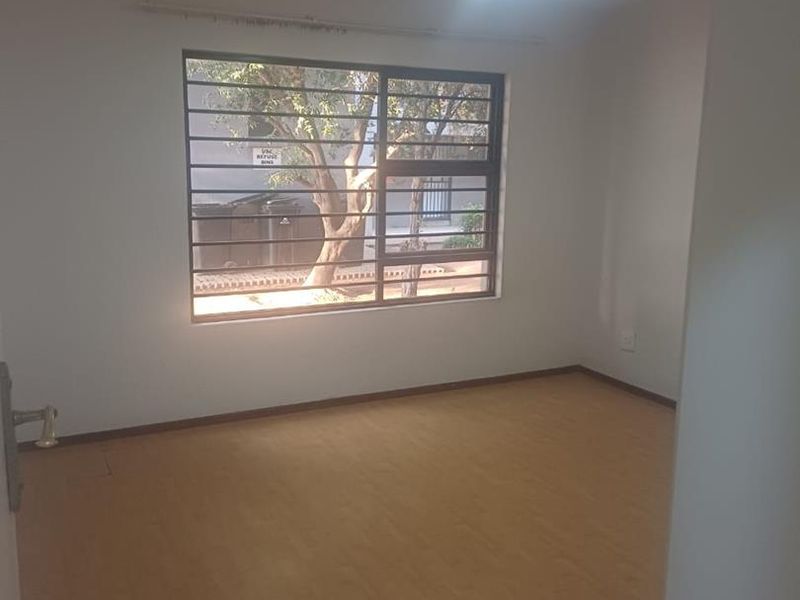 An empty bedroom featuring laminate flooring and a large window fitted with security bars, offering a bright and neutral space.