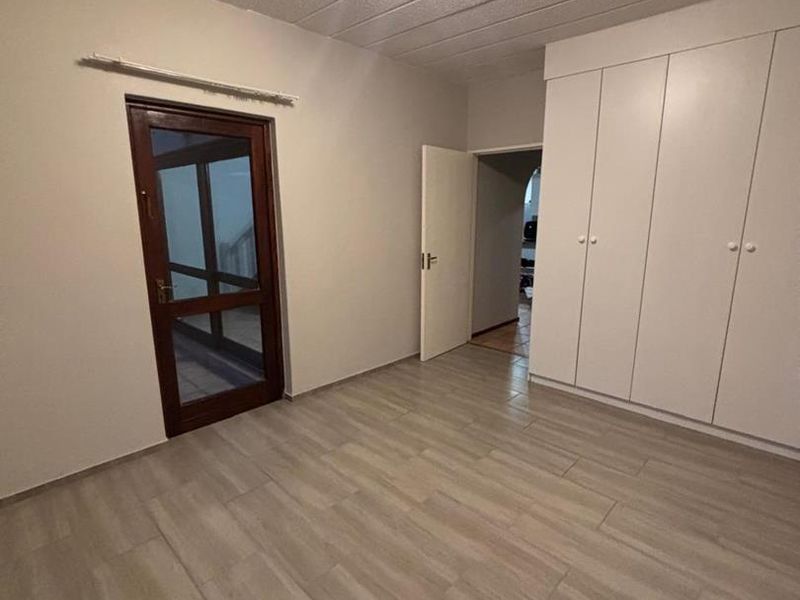 A clean, empty bedroom featuring neutral tiled flooring, built-in cupboards, and a textured ceiling, offering a versatile space ready for personalization.