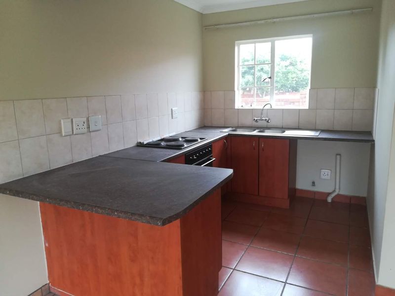 A functional kitchen featuring wooden cabinetry, dark laminate countertops, a built-in oven and hob, and tiled flooring.