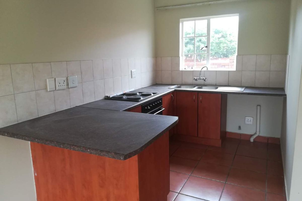 A functional kitchen featuring wooden cabinetry, dark laminate countertops, a built-in oven and hob, and tiled flooring.