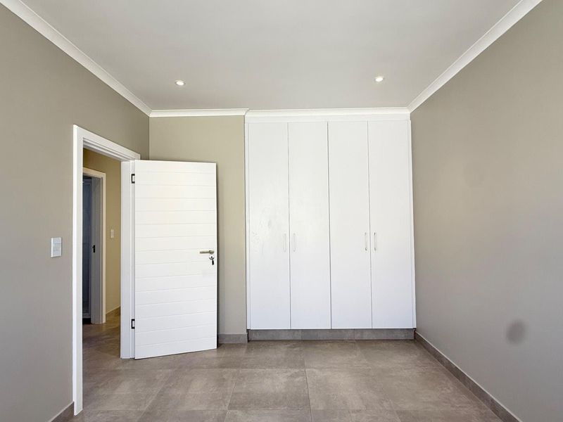 A clean, modern bedroom featuring neutral wall tones, large-format floor tiles, and ample built-in cupboard storage.