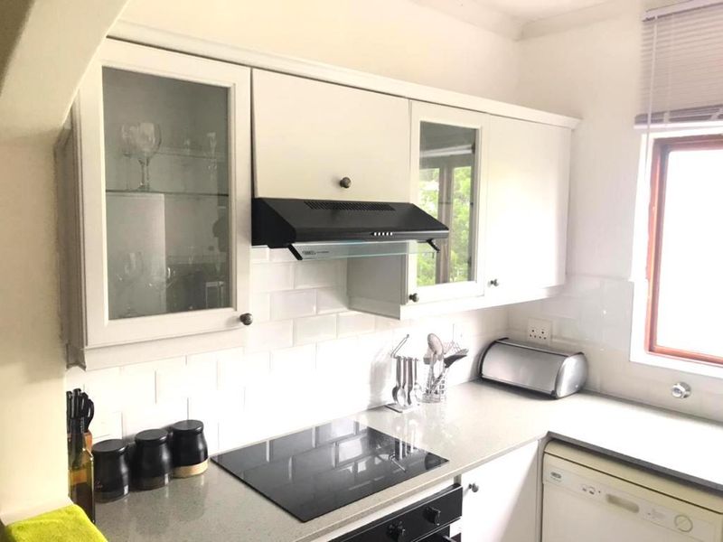 A well-maintained kitchen featuring white cabinetry, subway tile backsplash, stone countertops, and integrated appliances including an electric hob and extractor fan.
