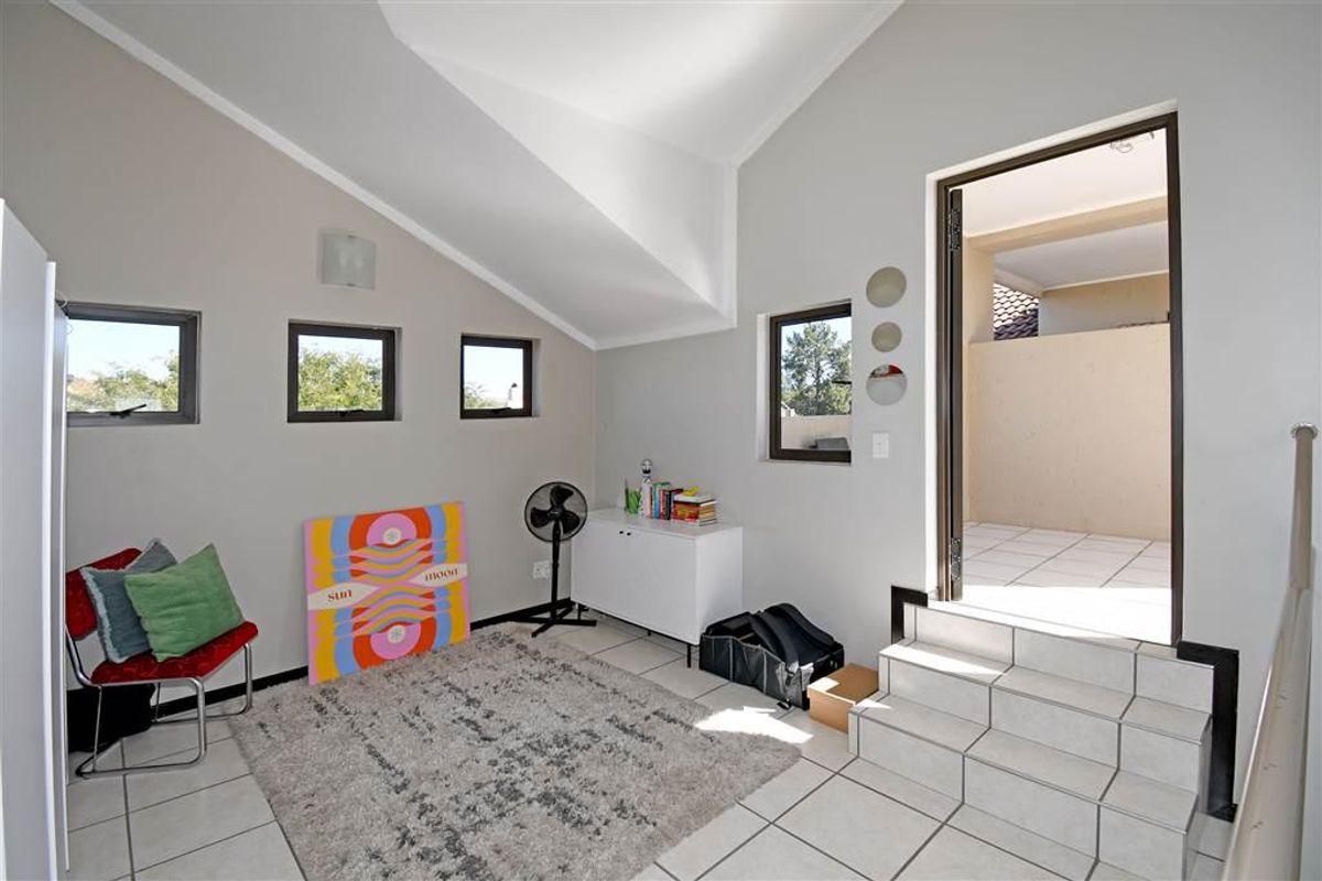 A bright living area featuring vaulted ceilings, tiled flooring, and direct access to an outdoor patio area via a small set of tiled steps.