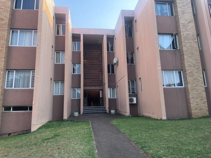 Front elevation of a multi-story apartment building featuring a central entrance, brick and painted facade, and paved walkway access.