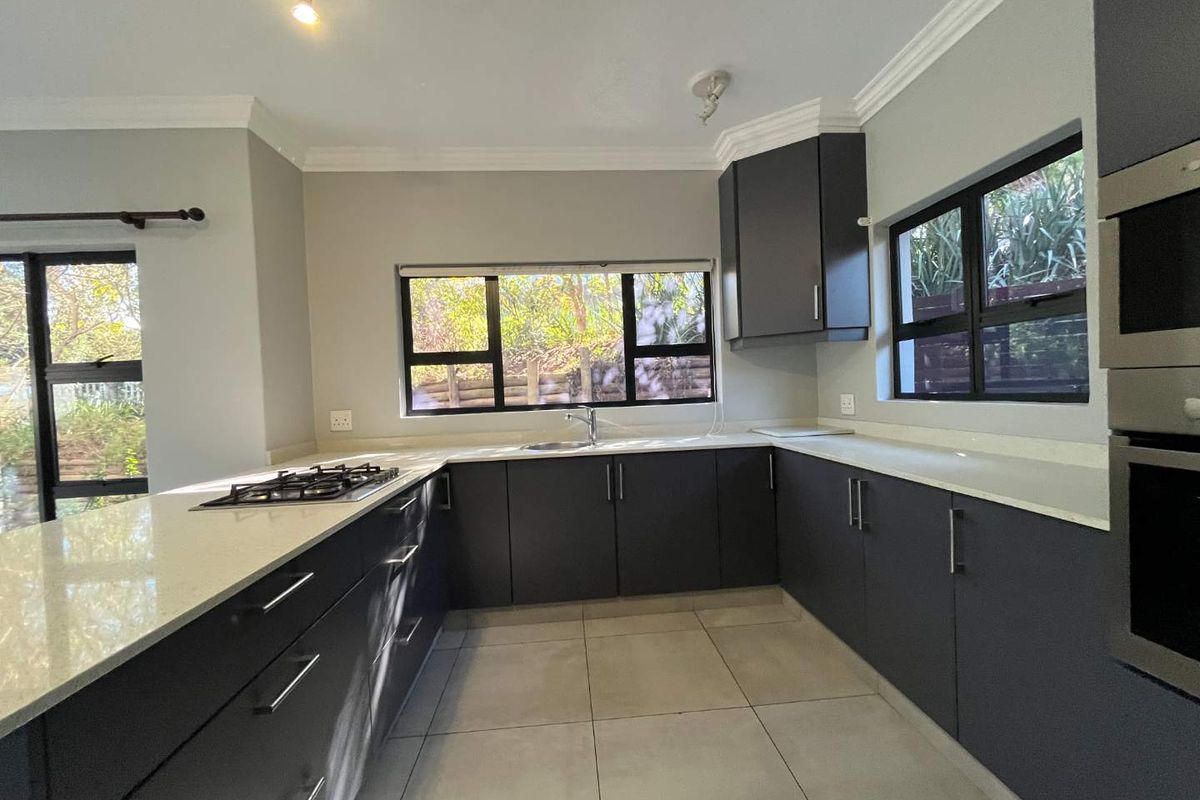 Modern kitchen featuring dark cabinetry, quartz countertops, a gas hob, built-in oven, and microwave, with large windows providing natural light and garden views.