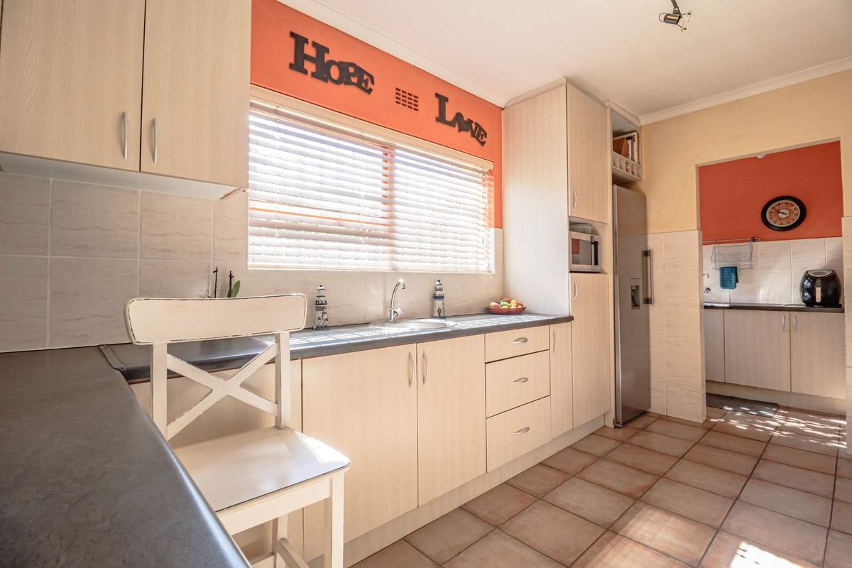 A functional kitchen featuring light wood-finish cabinetry, tiled flooring, a stainless steel sink, and a built-in microwave space, with an adjacent scullery area.