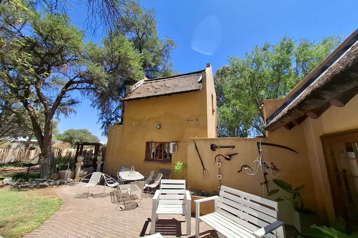 A charming rear patio area featuring a paved courtyard, thatched roof architecture, and mature garden surroundings, ideal for outdoor relaxation.