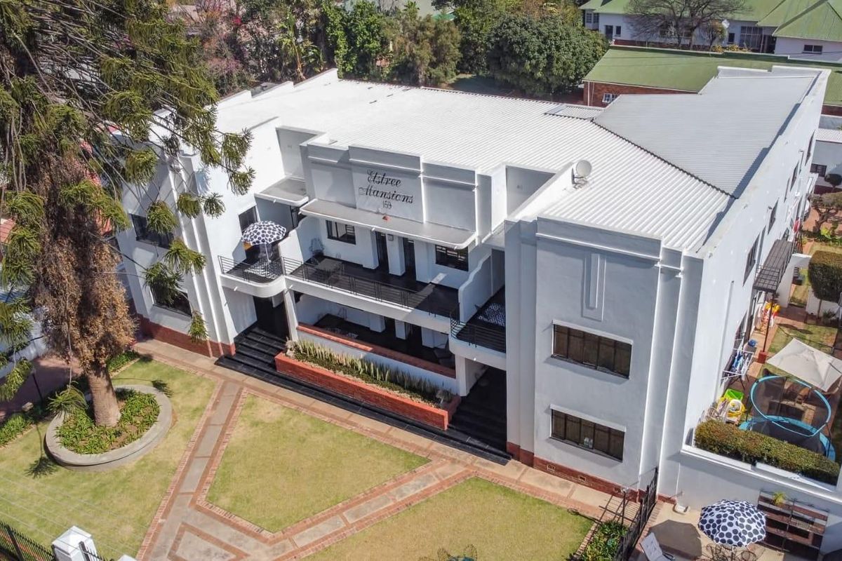 Aerial view of Elstree Mansions, showcasing the building's architectural facade, metal roofing, balconies, and surrounding landscaped garden areas.