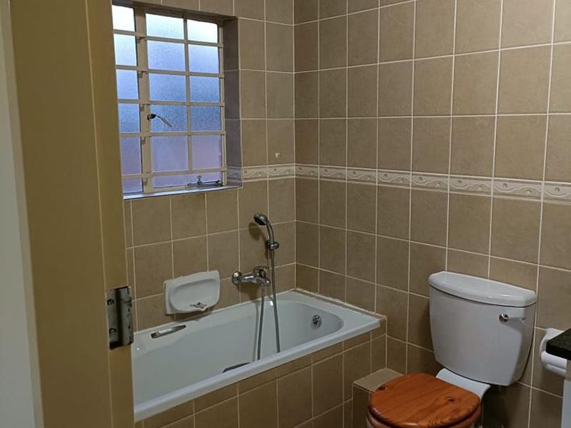 A functional bathroom featuring a built-in bathtub with shower mixer, toilet, and neutral floor-to-ceiling wall tiling.