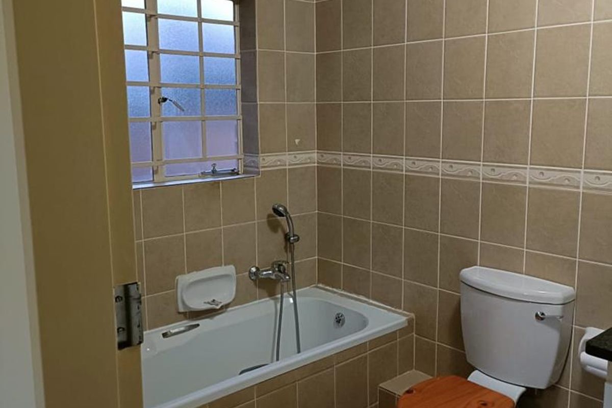 A functional bathroom featuring a built-in bathtub with shower mixer, toilet, and neutral floor-to-ceiling wall tiling.