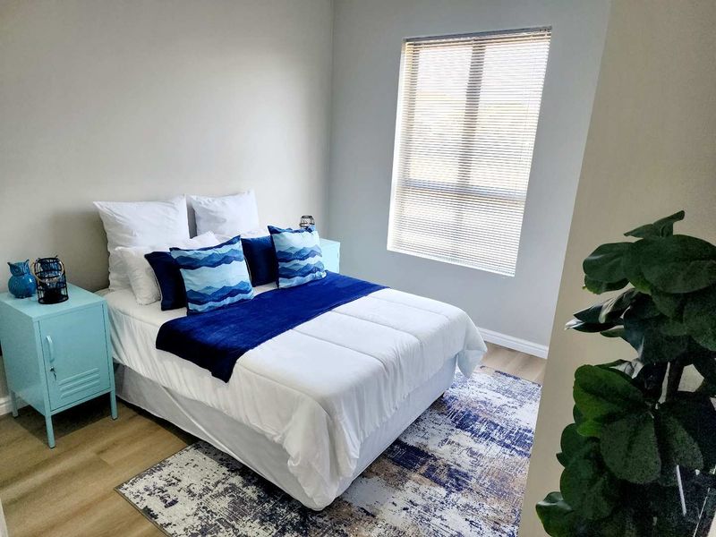 A well-lit bedroom featuring neutral walls, laminate flooring, and a window fitted with venetian blinds.
