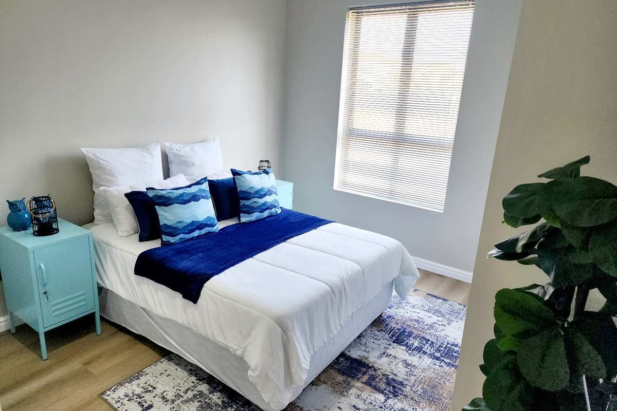 A well-lit bedroom featuring neutral walls, laminate flooring, and a window fitted with venetian blinds.