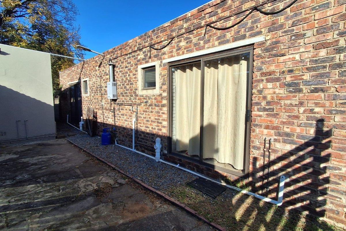 Rear exterior view of the property featuring exposed brickwork, a sliding glass door, and external utility installations including a gas geyser.