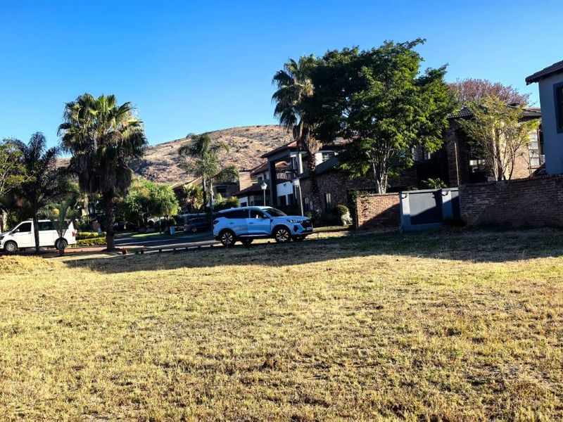 A vacant residential plot situated in a developed estate, featuring established boundary walls and surrounding residential properties.