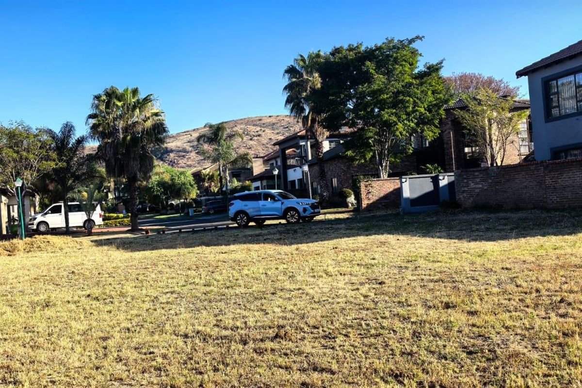A vacant residential plot situated in a developed estate, featuring established boundary walls and surrounding residential properties.