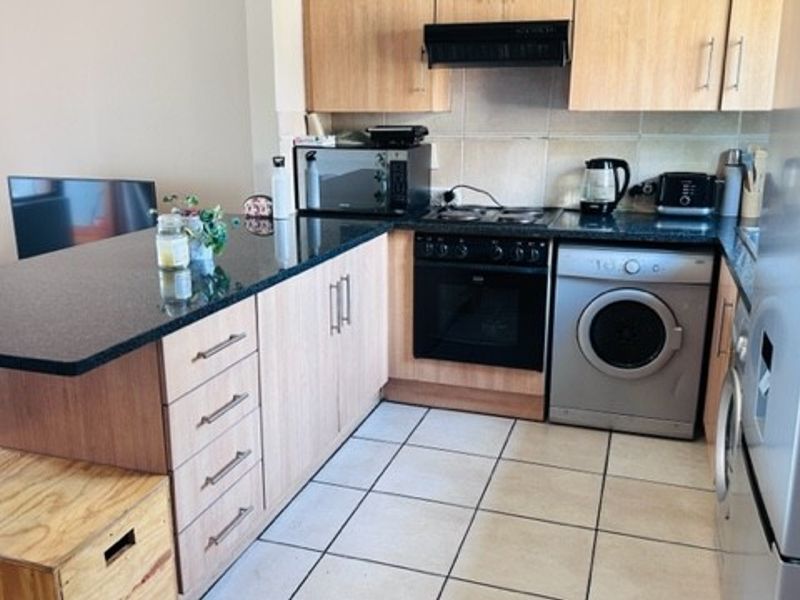 A functional kitchen featuring light wood cabinetry, dark granite countertops, tiled flooring, and built-in appliances including an oven, hob, and washing machine.