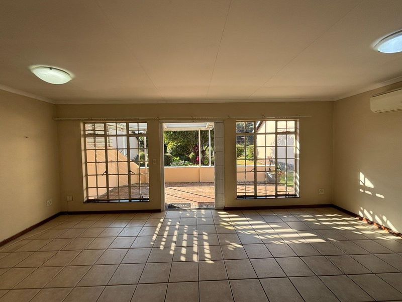 Spacious, sunlit living area featuring neutral tiled flooring, large grid-pattern windows, and direct access to an outdoor patio space.