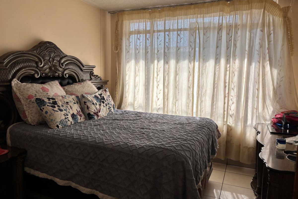 A bedroom featuring tiled flooring and large windows with curtain tracks. The room shows signs of wear including ceiling and wall finish deterioration.