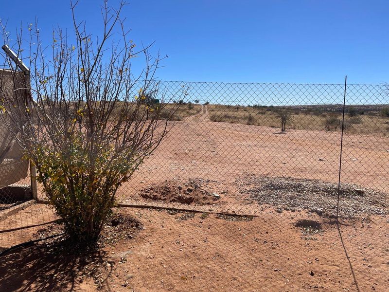 An outdoor area featuring a chain-link fence boundary overlooking a dry, undeveloped landscape.