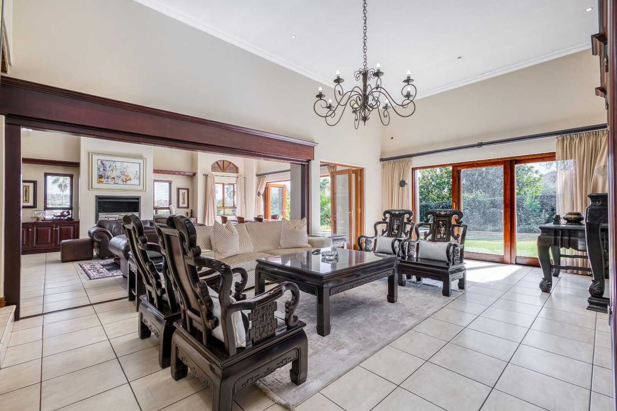 Spacious living room featuring tiled flooring, a vaulted ceiling, a decorative chandelier, and large sliding glass doors providing access to the garden.