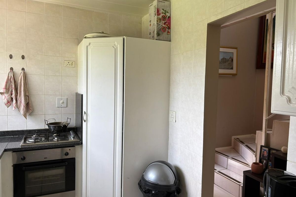 A functional kitchen featuring built-in oven, gas hob, granite countertops, and tiled wall finishes, providing a practical workspace with direct access to the staircase.