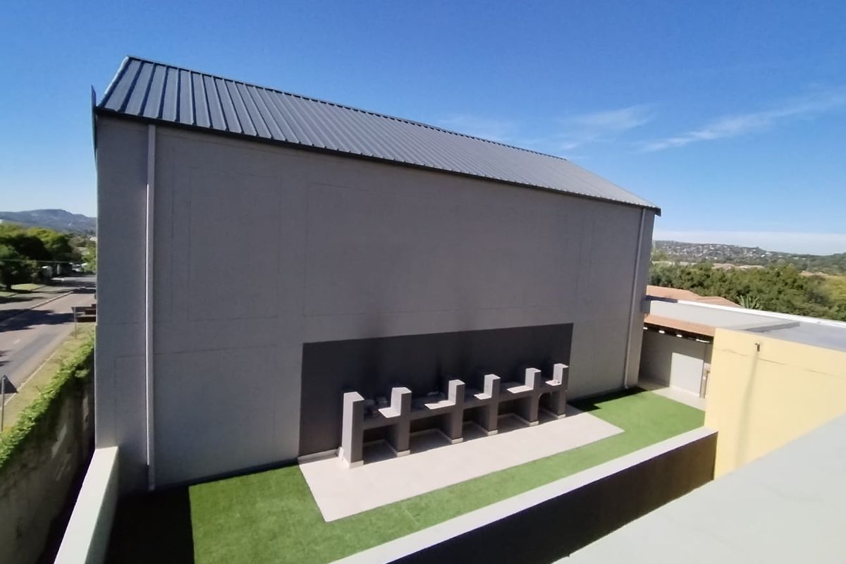 Rear exterior view featuring a row of built-in braai stations, artificial lawn, and a paved patio area under a metal roof.