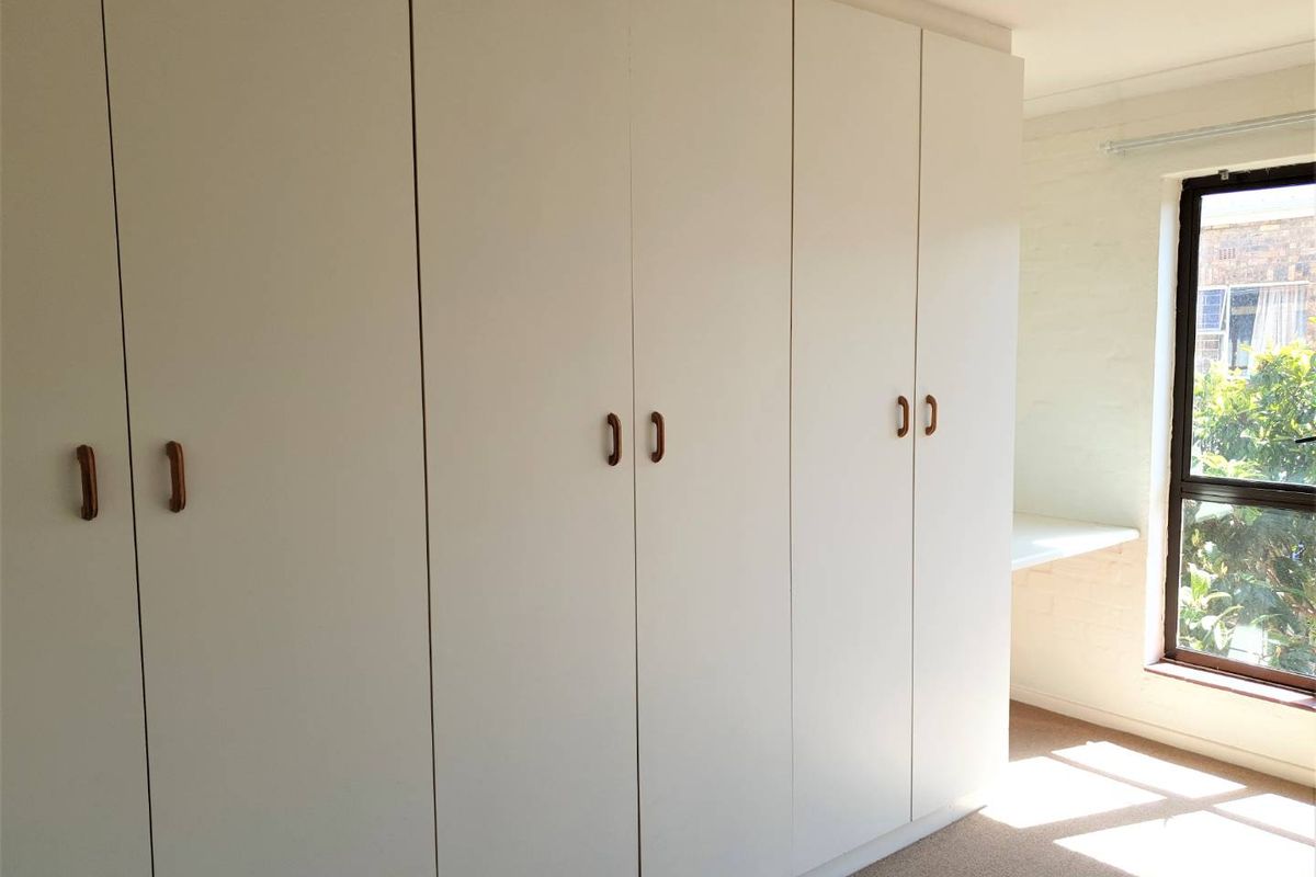A bright bedroom featuring extensive floor-to-ceiling built-in wardrobes and a convenient built-in desk area by the window.