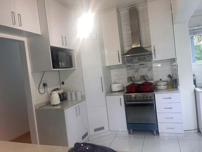 Modern kitchen featuring white cabinetry, stone countertops, subway tile backsplash, and stainless steel appliances, including a built-in microwave and extractor fan.