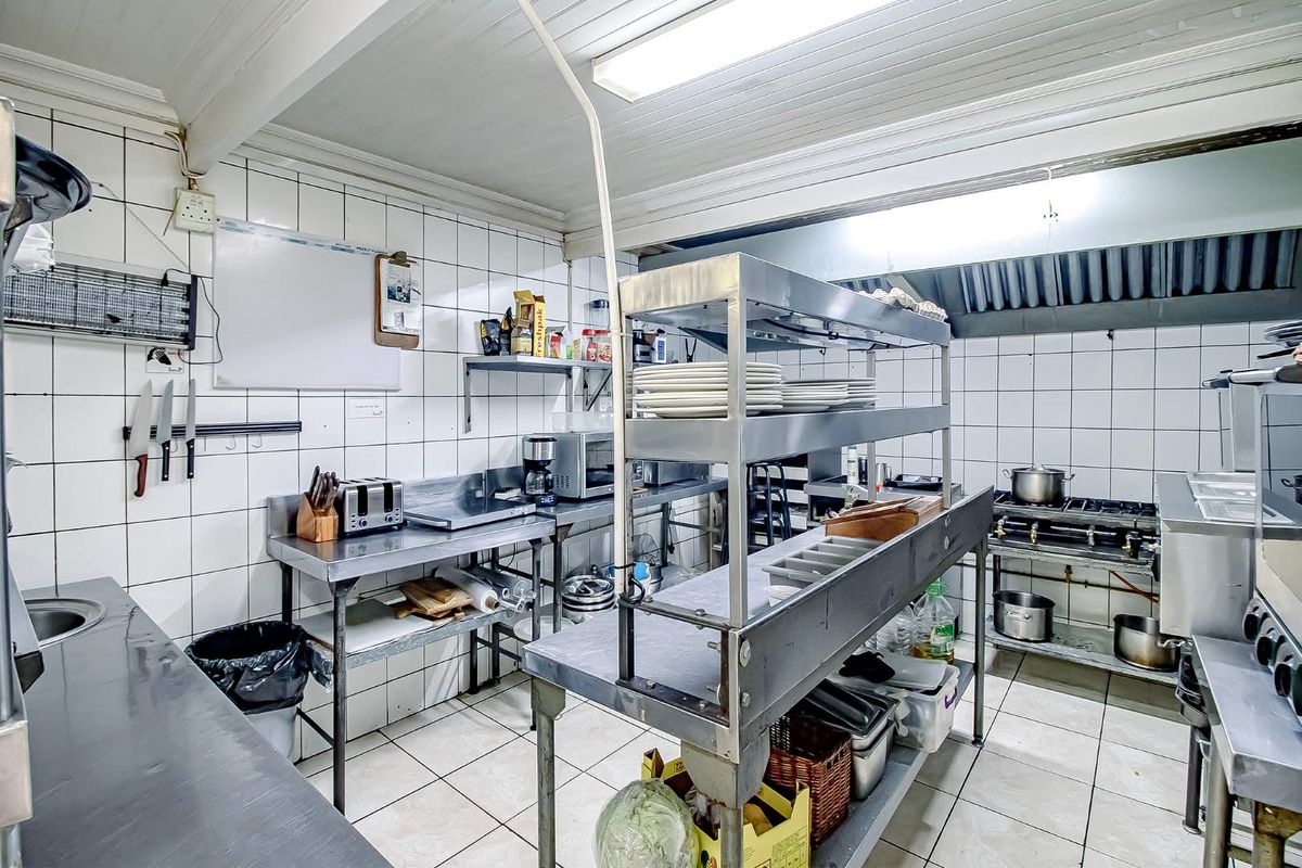 A functional commercial-style kitchen featuring stainless steel prep tables, tiled walls, and industrial-grade shelving, designed for efficient food preparation and service.