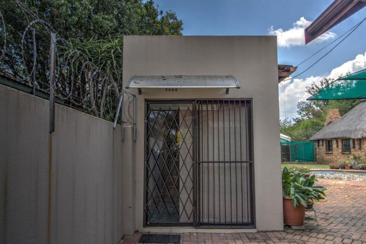 Rear exterior view showing a paved patio area, security gate, and boundary wall with razor wire fencing.