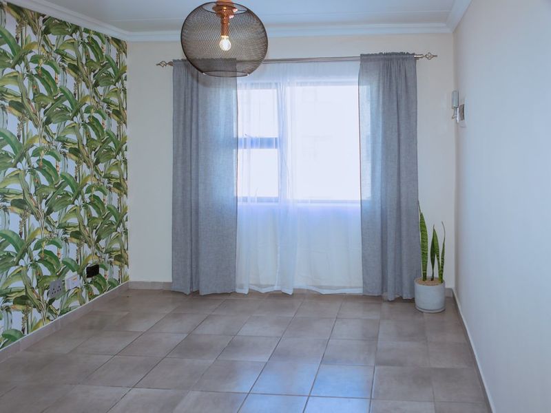 A bright, empty bedroom featuring neutral tiled flooring, a decorative botanical feature wall, and coving detail.
