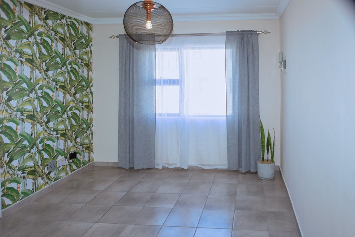 A bright, empty bedroom featuring neutral tiled flooring, a decorative botanical feature wall, and coving detail.
