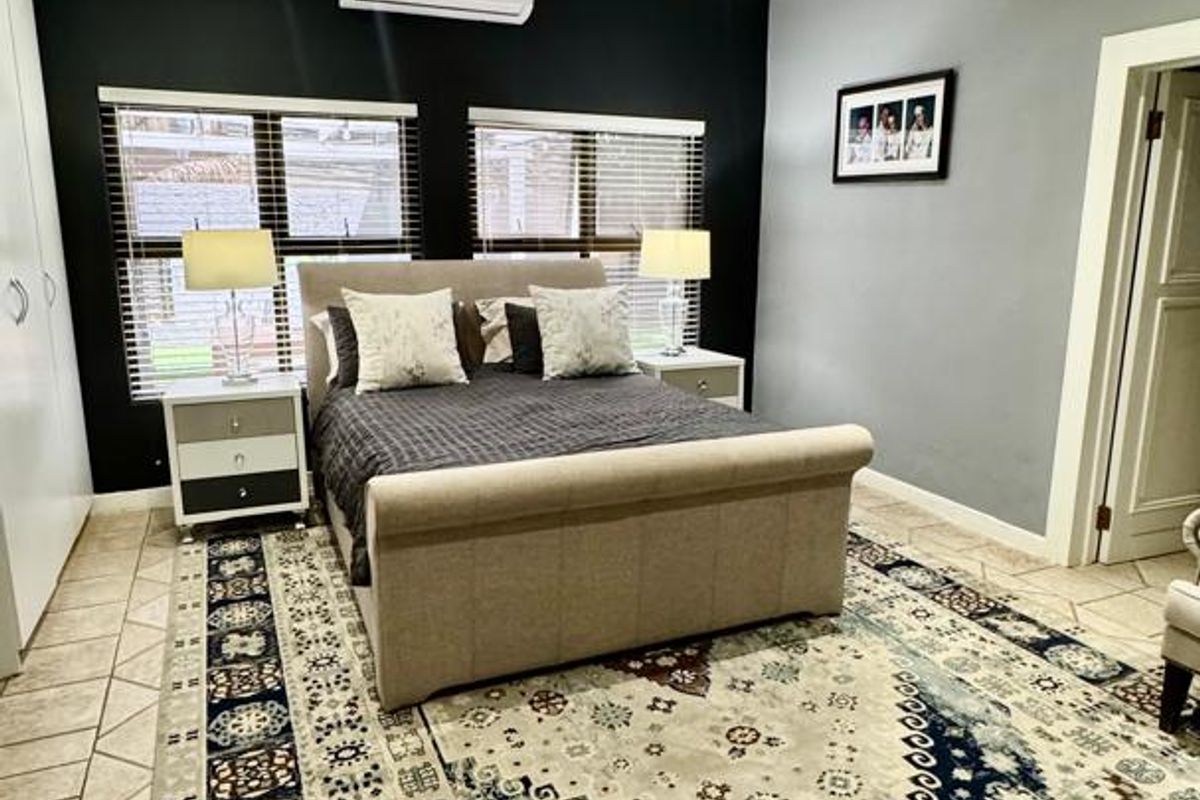 A well-maintained bedroom featuring tiled flooring, recessed ceiling lighting, and a wall-mounted air conditioning unit.