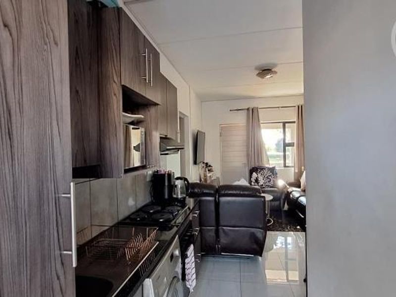 Open plan kitchen and living area featuring modern dark wood cabinetry, gas hob, extractor fan, and tiled flooring throughout.