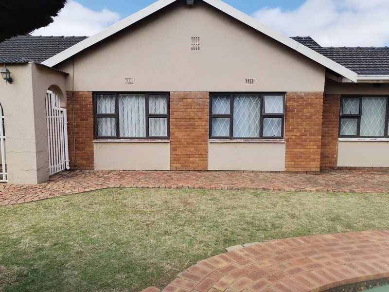 Rear view of the house featuring a brick and plaster facade, tiled roof, security-barred windows, and a paved walkway leading to the lawn.
