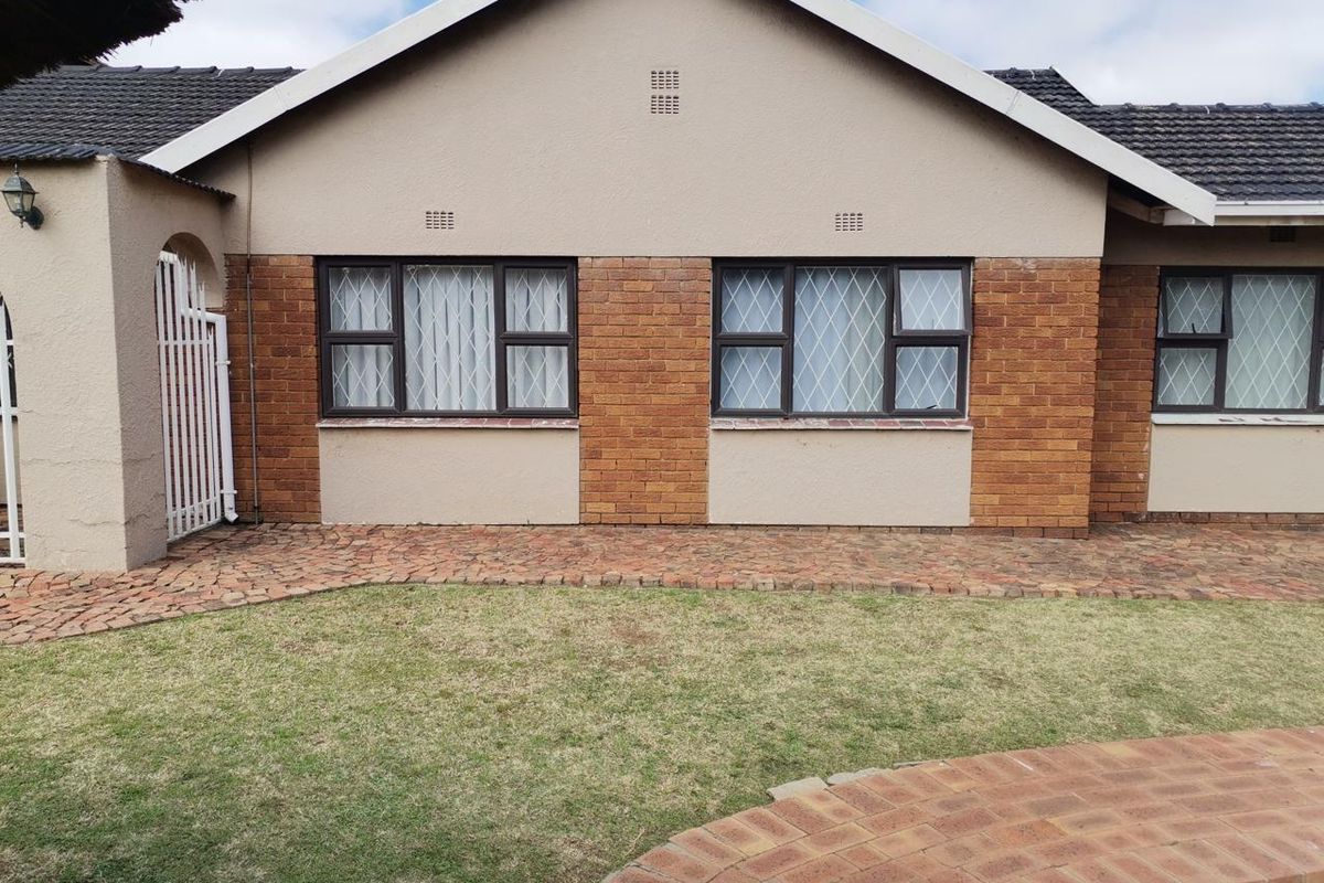 Rear view of the house featuring a brick and plaster facade, tiled roof, security-barred windows, and a paved walkway leading to the lawn.