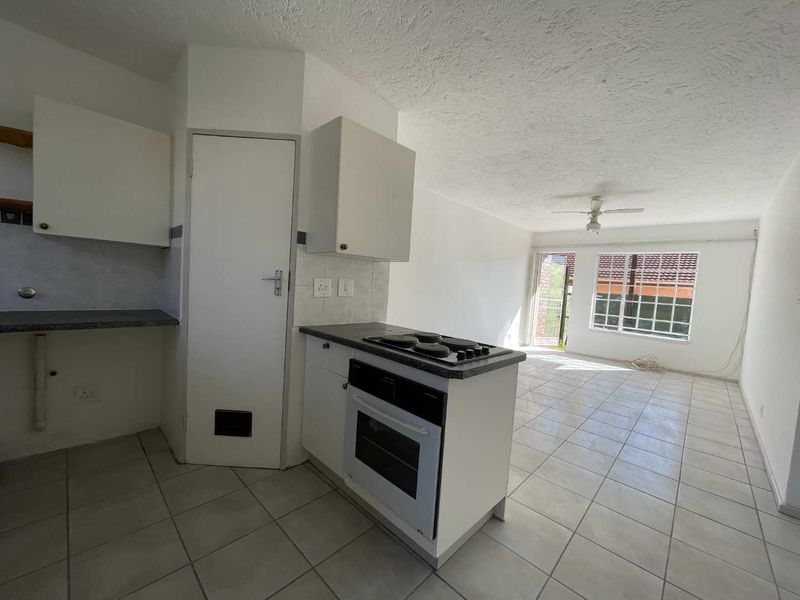 An open-plan kitchen and living area featuring tiled floors, built-in cabinetry, an integrated oven and hob, and a ceiling fan.