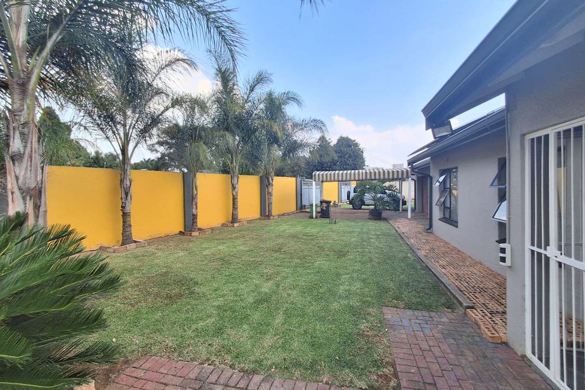 A spacious rear garden featuring a well-maintained lawn, perimeter boundary wall, and paved walkway alongside the house exterior.